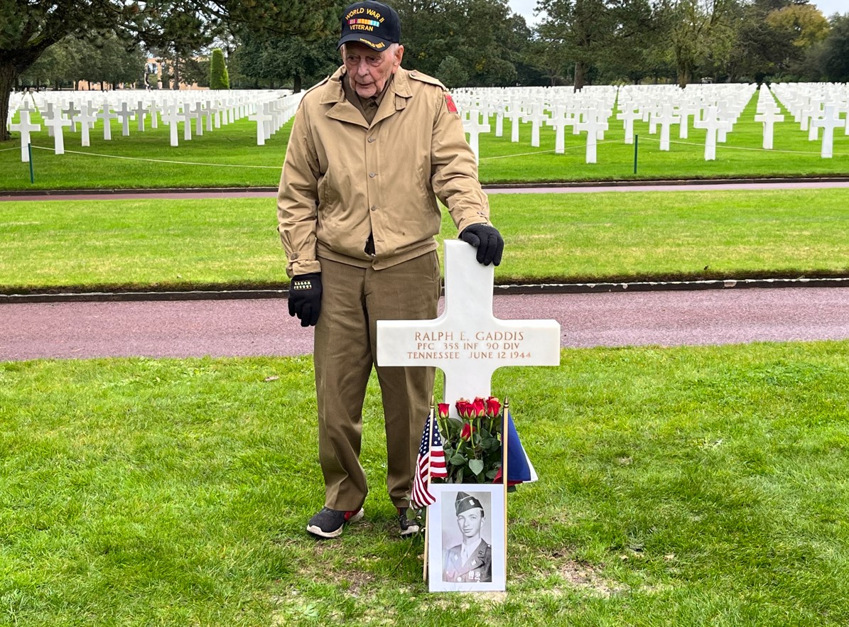 Eugene “Gene” Kleindl near his friend’s headstone at Normandy American Cemetery. Credits: ABMC.