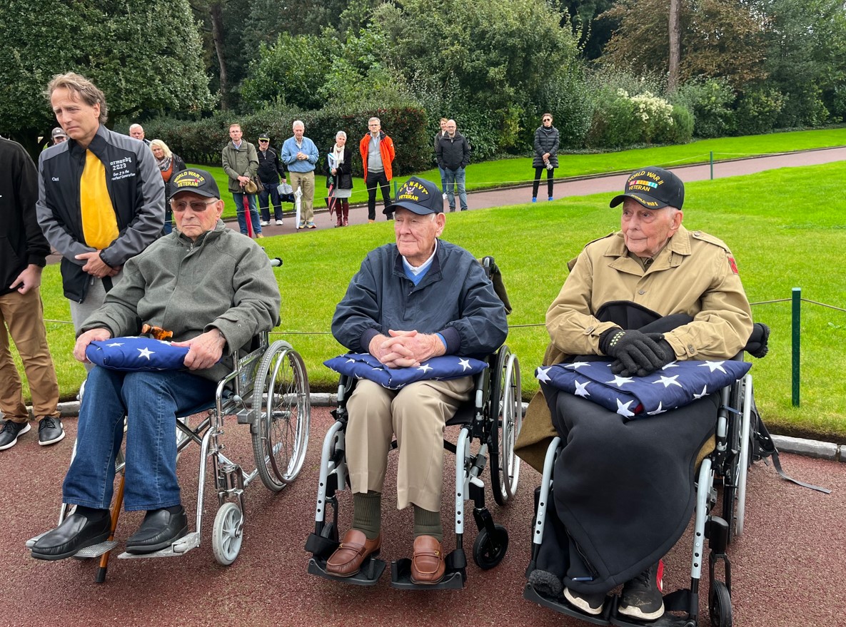 The two World War II U.S. veterans, William “Magic Bill” Hunter (in the middle) and Eugene “Gene” Kleindl (on the right) with Jean Turco, former French prisoner of war in Germany (on the left) at the flagpole at Normandy American Cemetery after the lowering of the flag. Credits: ABMC.