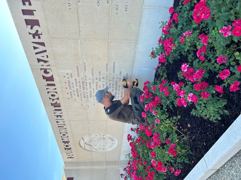 A man drills a hole in a stone wall at Epinal American Cemetery 