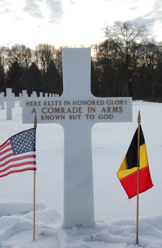 Unknown headstone under the snow with U.S. and Belgian flags. Credits: American Battle Monuments Commission. 