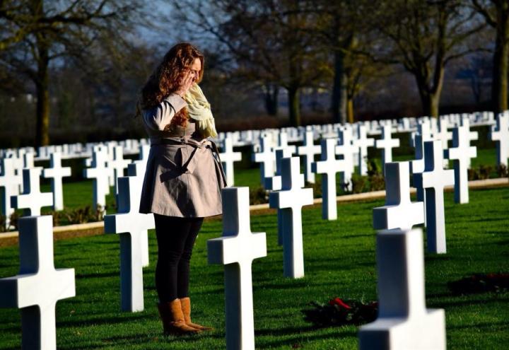 A woman salutes a headstone with a wreath. 