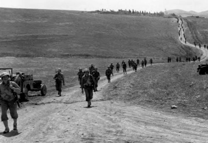 American infantry march down a dirt road. 