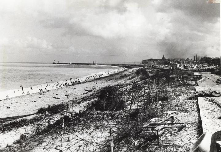 This historic image shows concrete barriers, wire fencing, and other obstacles on the beach. 