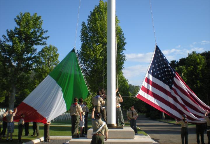 Boy Scouts raise large Italian and American flags on a flag pole.