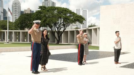 Vicente Lim IV (Vincci) Manila Visitor Center Director and Commandant of the Marine Corps General Eric M. Smith and Sergeant Major of the Marine Corps Carlos A. Ruiz and their spouses participating in a salute at the Manila American Cemetery and Memorial, with skyscrapers in the background.