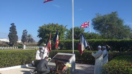 Caveness bends down to lay a wreath at the base of the marker. 
