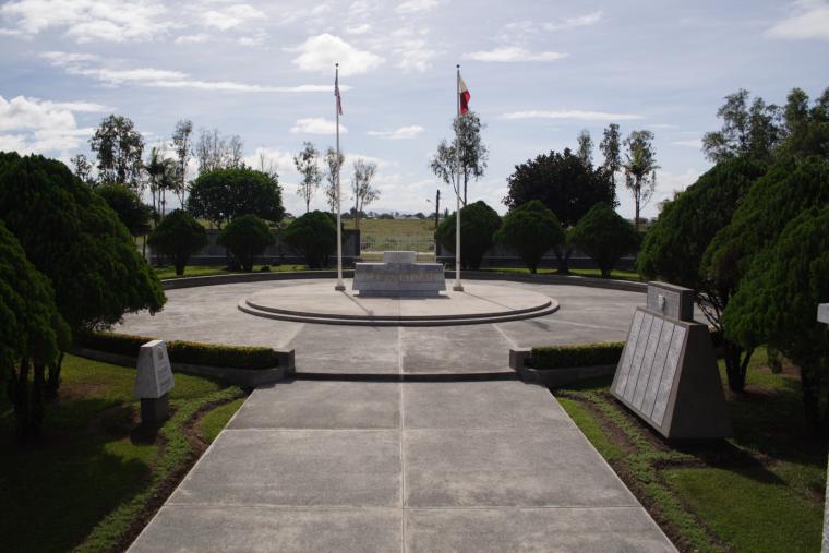 A distant view of the Cabanatuan American Memorial shows the entire plaza including a concrete pathway and two flags poles.