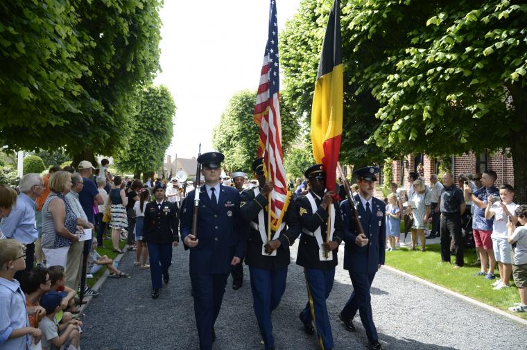 Men in uniform march with flags or firearms as part of the Honor Guard.