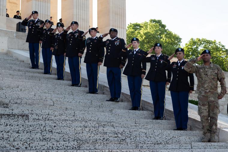 Soldiers in uniform stand on the steps of the monument and salute. 